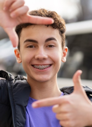 Boy with braces and purple shirt posing his hands to frame his face.