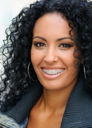 Brown-haired-girl with hoop earrings smiling wearing braces.