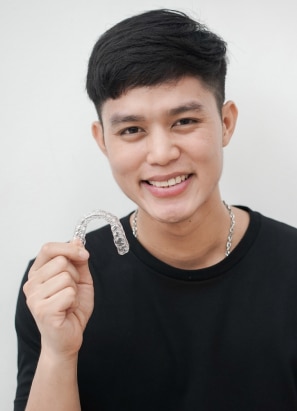 Young person with short hair and black shirt holding up Invisalign.