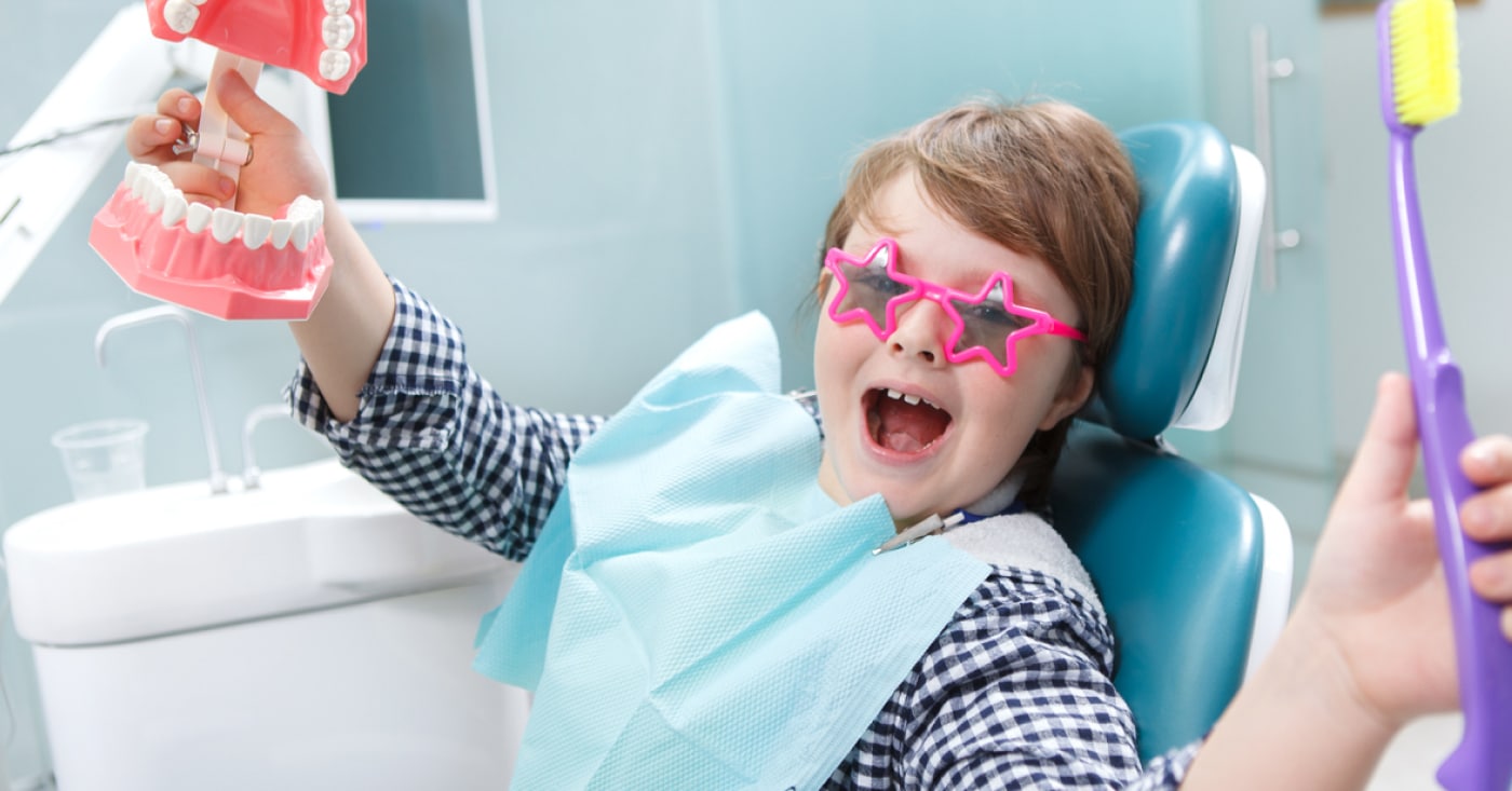 Smiling kid in dentist office chair with pink-star-shaped-dental-glasses.