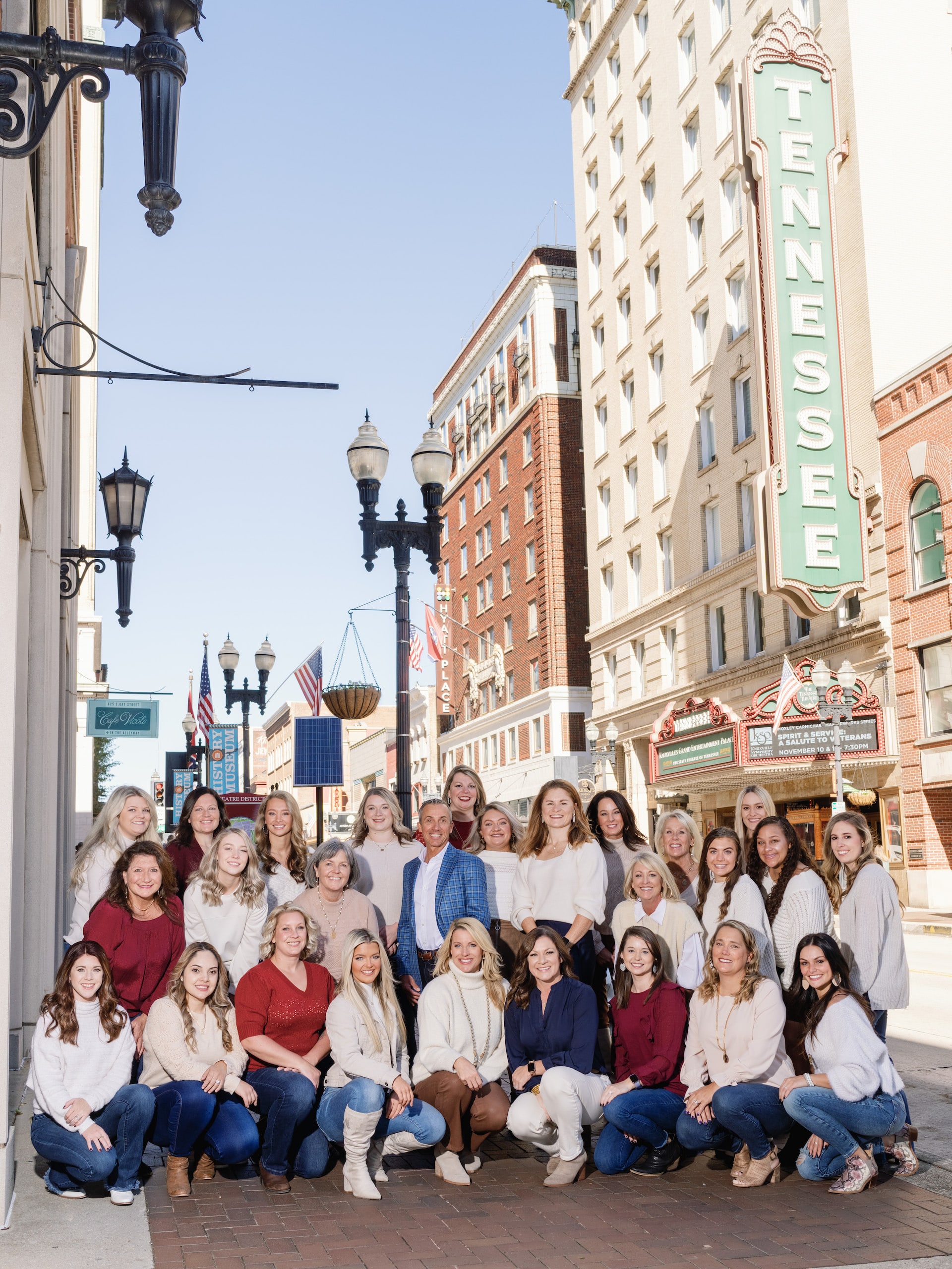 A group of people gathered on a street near the Tennessee Theatre, with vintage lampposts and blue sky in the background.