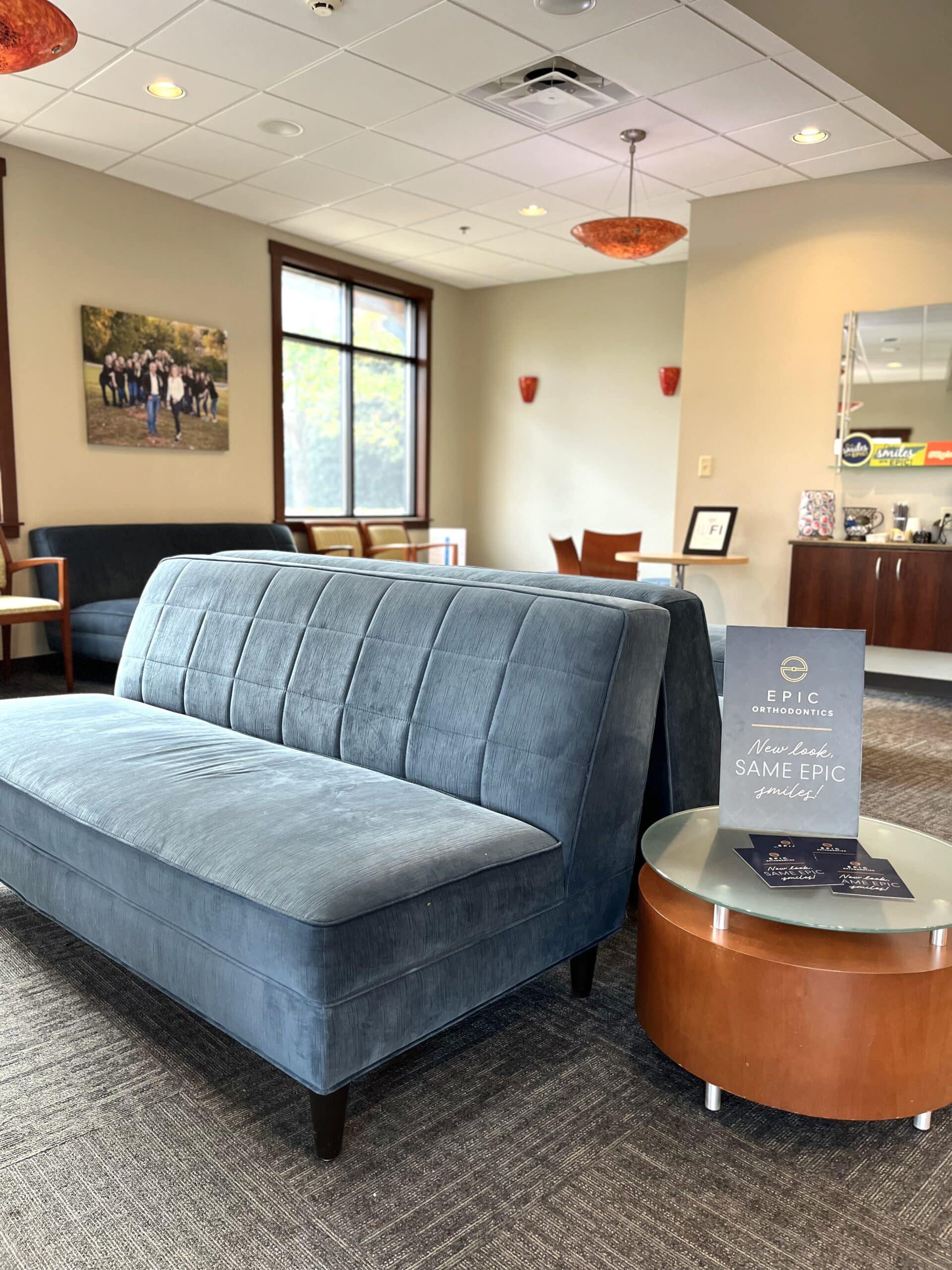 A waiting room with blue seating, modern decor, and artwork on the wall. A sign displays "Epic Orthodontics."