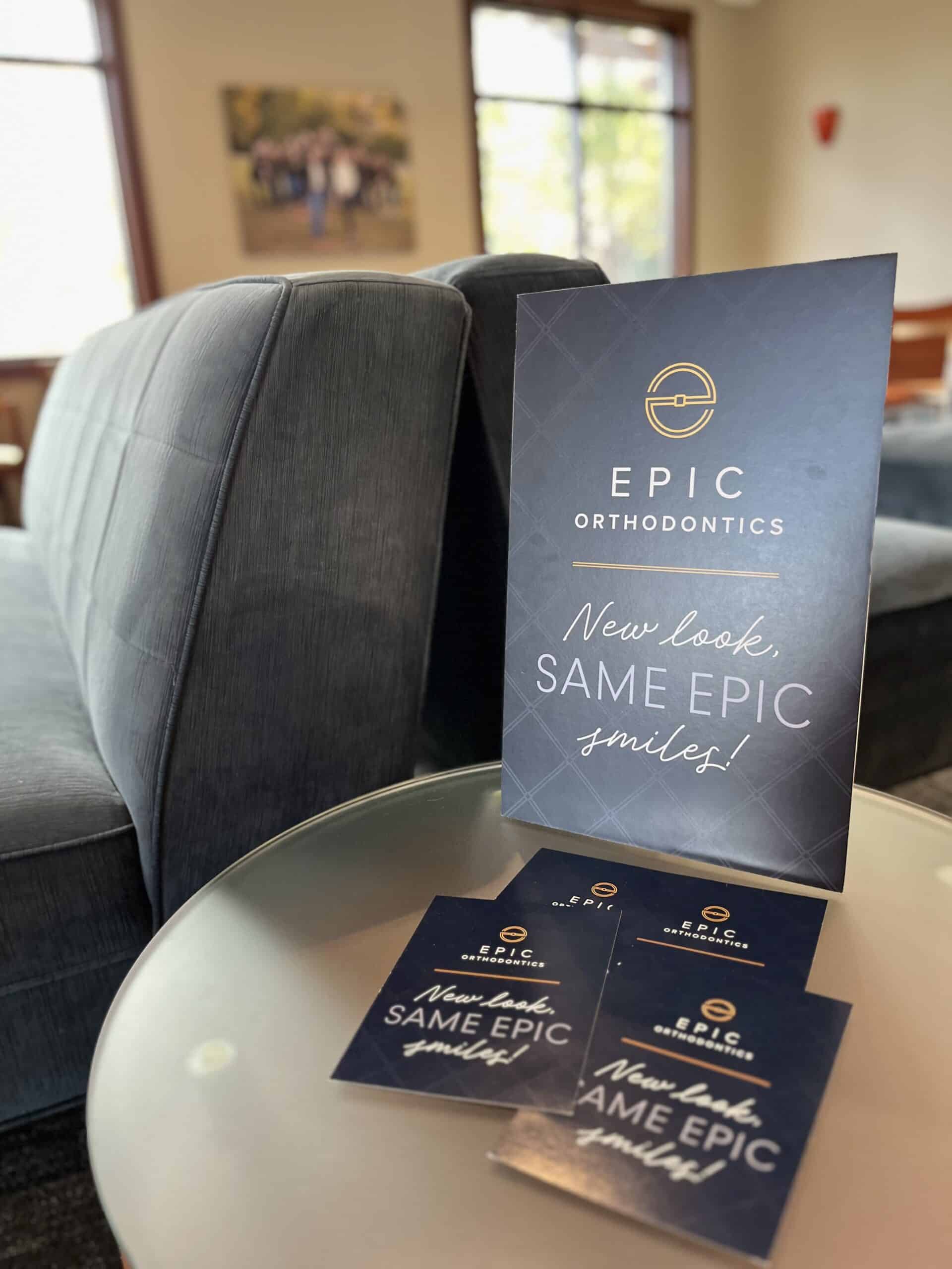 A modern orthodontics clinic interior with promotional materials on a glass table. A couch is visible, and a wall photo hangs nearby.