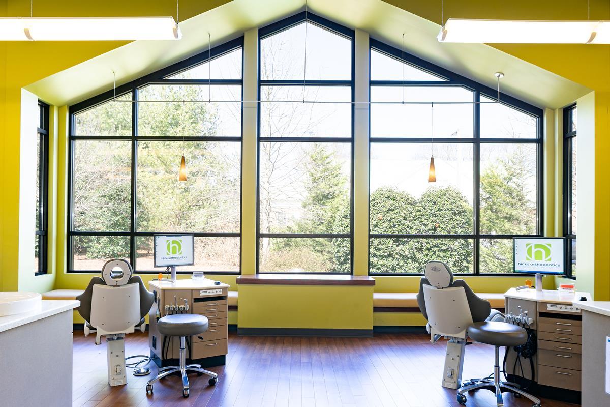 Bright dental office with large windows, yellow walls, and modern equipment. Outdoor greenery visible through glass, creating a welcoming and fresh atmosphere.